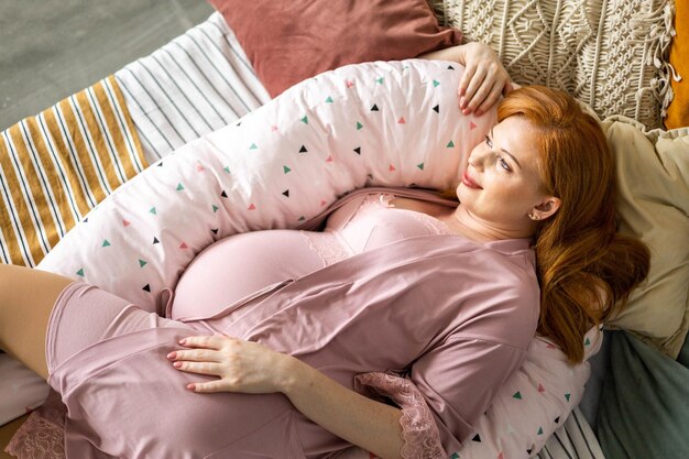 Pregnant women lying on comfortable bed hugging pregnancy pillow